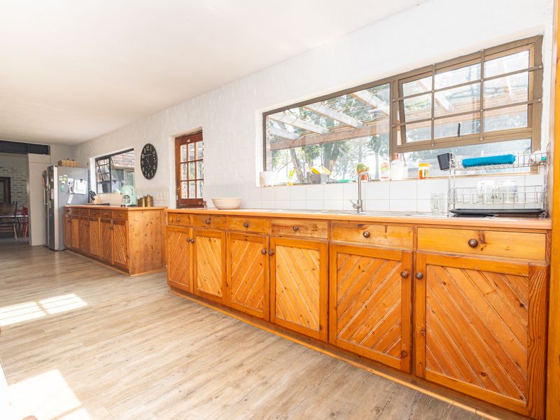 Spacious kitchen featuring extensive wooden cabinetry, a stainless steel sink, tiled backsplash, and durable laminate flooring with natural light.