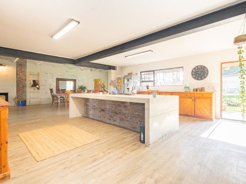 Spacious open-plan living and kitchen area featuring exposed steel beams, a unique concrete island, and rustic brick accents with timber cabinetry.