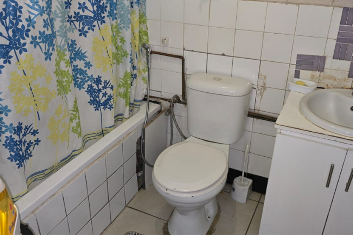 A dated bathroom featuring a bathtub, toilet, and vanity basin with visible wear to the tiling and exposed plumbing fixtures.