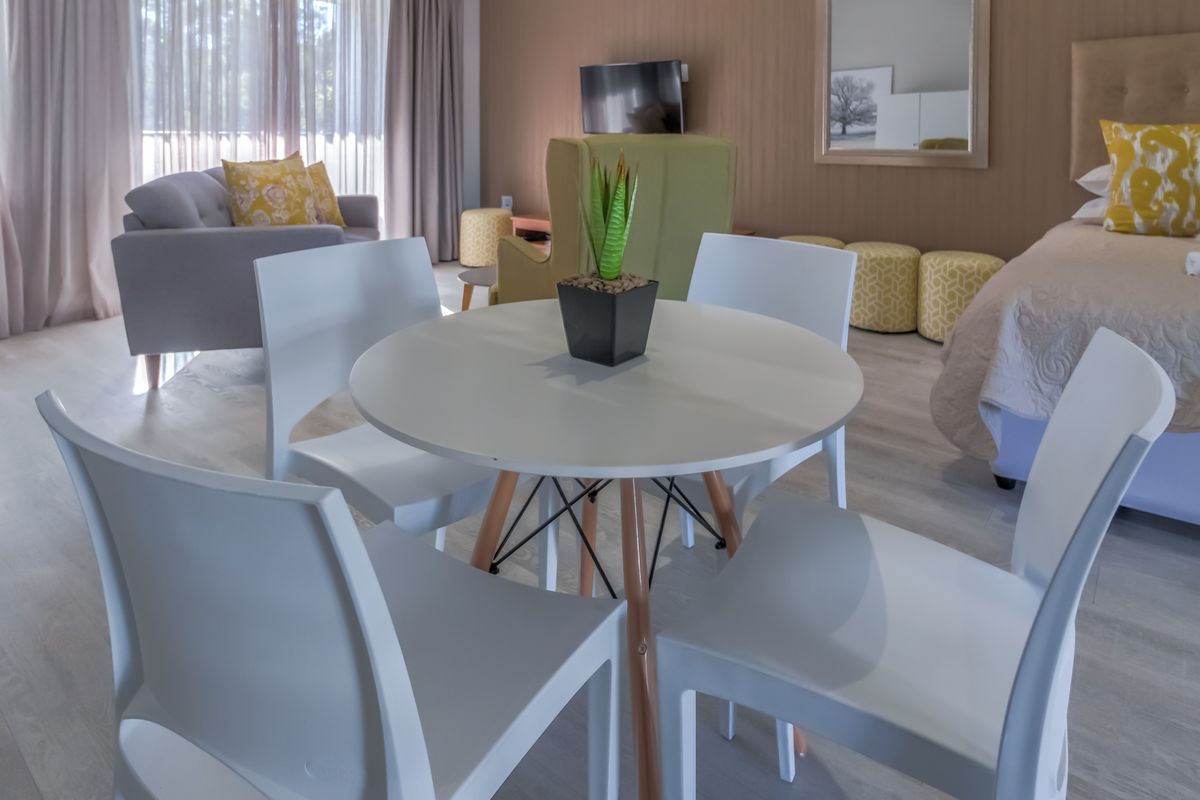 A well-maintained bedroom featuring light laminate flooring, neutral wall paneling, and floor-to-ceiling curtains providing ample natural light.