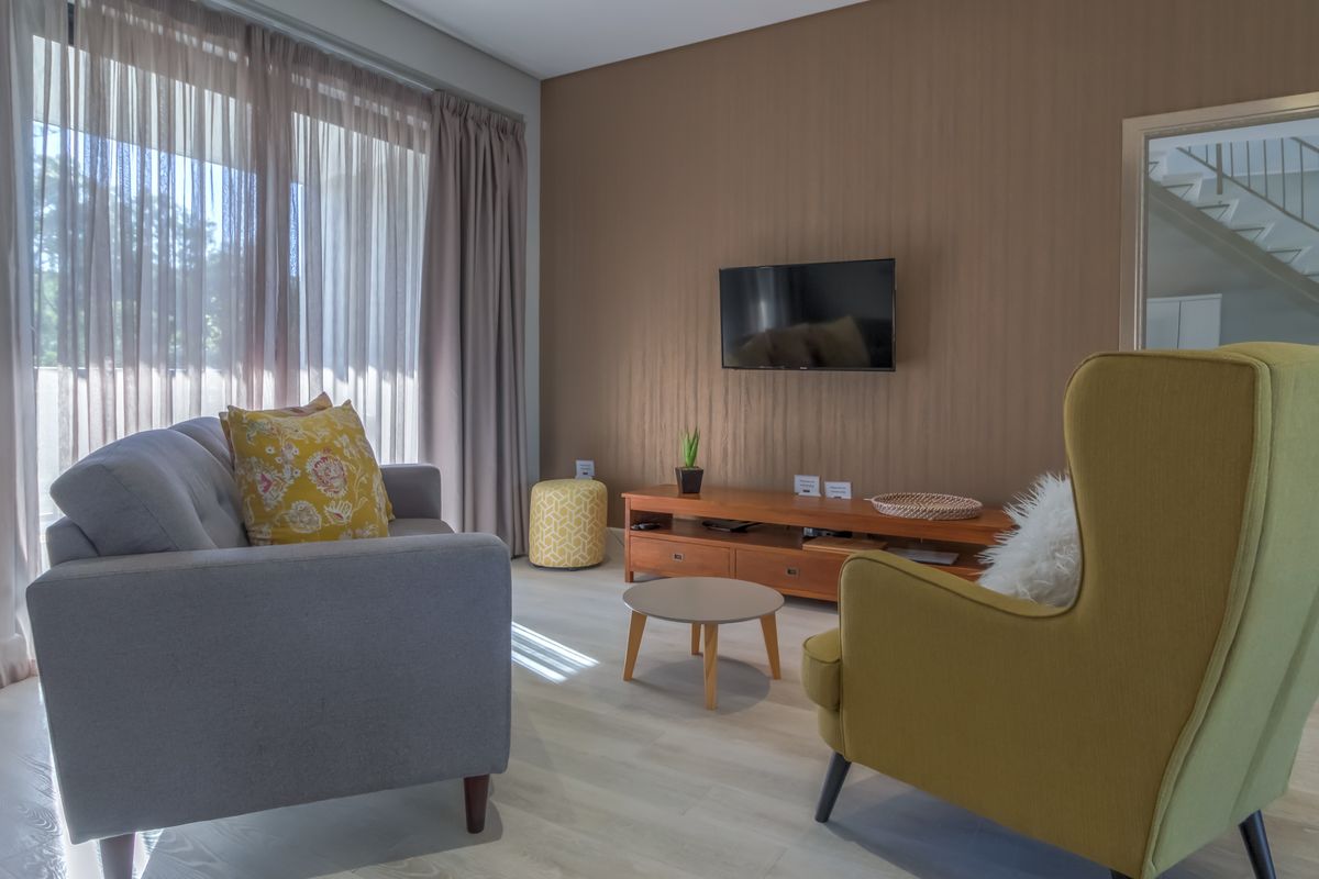 A well-lit living room featuring light-toned laminate flooring, neutral wall finishes, and large windows with floor-to-ceiling curtains.