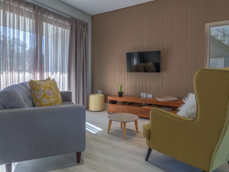 A well-lit living room featuring light-toned laminate flooring, neutral wall finishes, and large windows with floor-to-ceiling curtains.