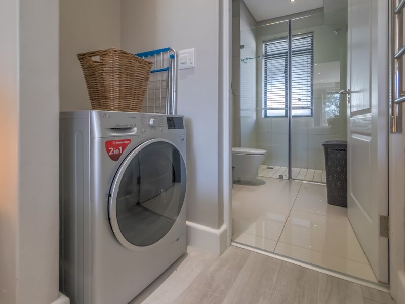 A compact laundry area featuring plumbing connections, adjacent to a modern bathroom with tiled floors and a glass-enclosed shower.