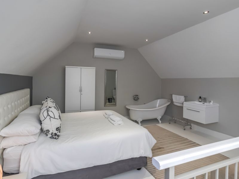 A spacious loft-style bedroom featuring a clawfoot bathtub and wall-mounted vanity, complemented by modern recessed lighting and a split-system air conditioner.