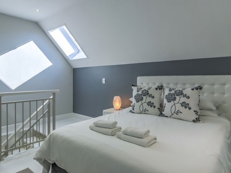 A bright attic bedroom featuring a skylight, modern railing, and a clean, contemporary aesthetic with neutral wall tones.