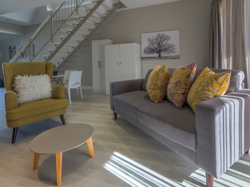 A bright living room featuring modern laminate flooring, a staircase, and built-in storage cupboards, creating a functional and open living space.