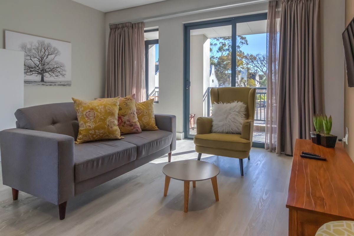 A bright and well-maintained living room featuring modern laminate flooring and large sliding glass doors that provide access to an outdoor balcony area.