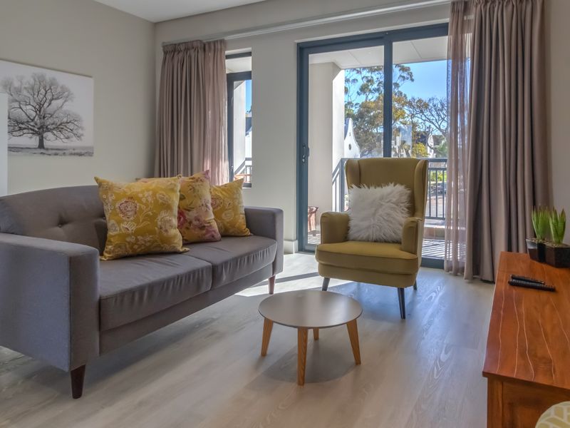 A bright and well-maintained living room featuring modern laminate flooring and large sliding glass doors that provide access to an outdoor balcony area.