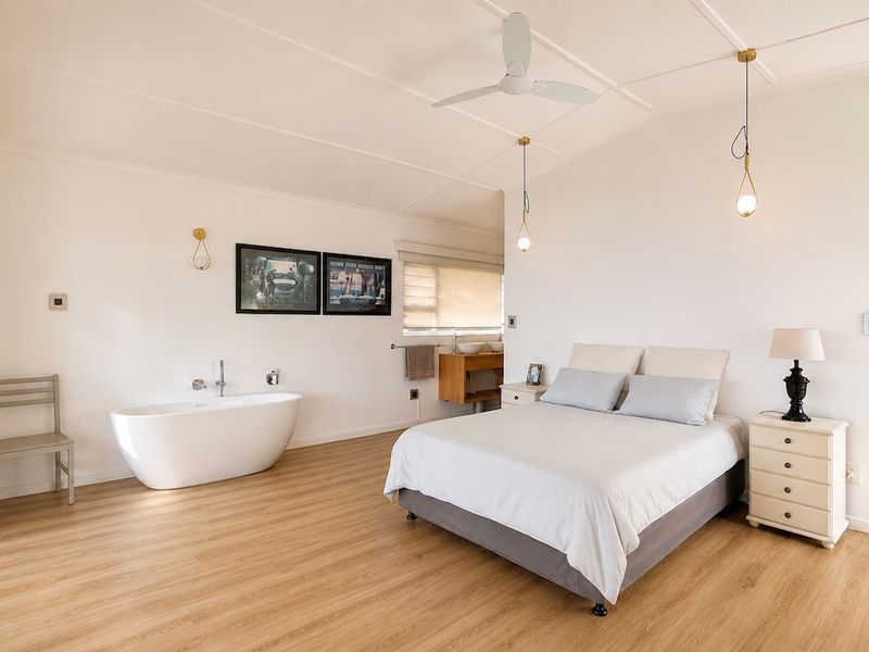 Spacious bedroom featuring a modern freestanding bathtub, built-in wardrobes, laminate flooring, and direct access to an outdoor area through sliding glass doors.