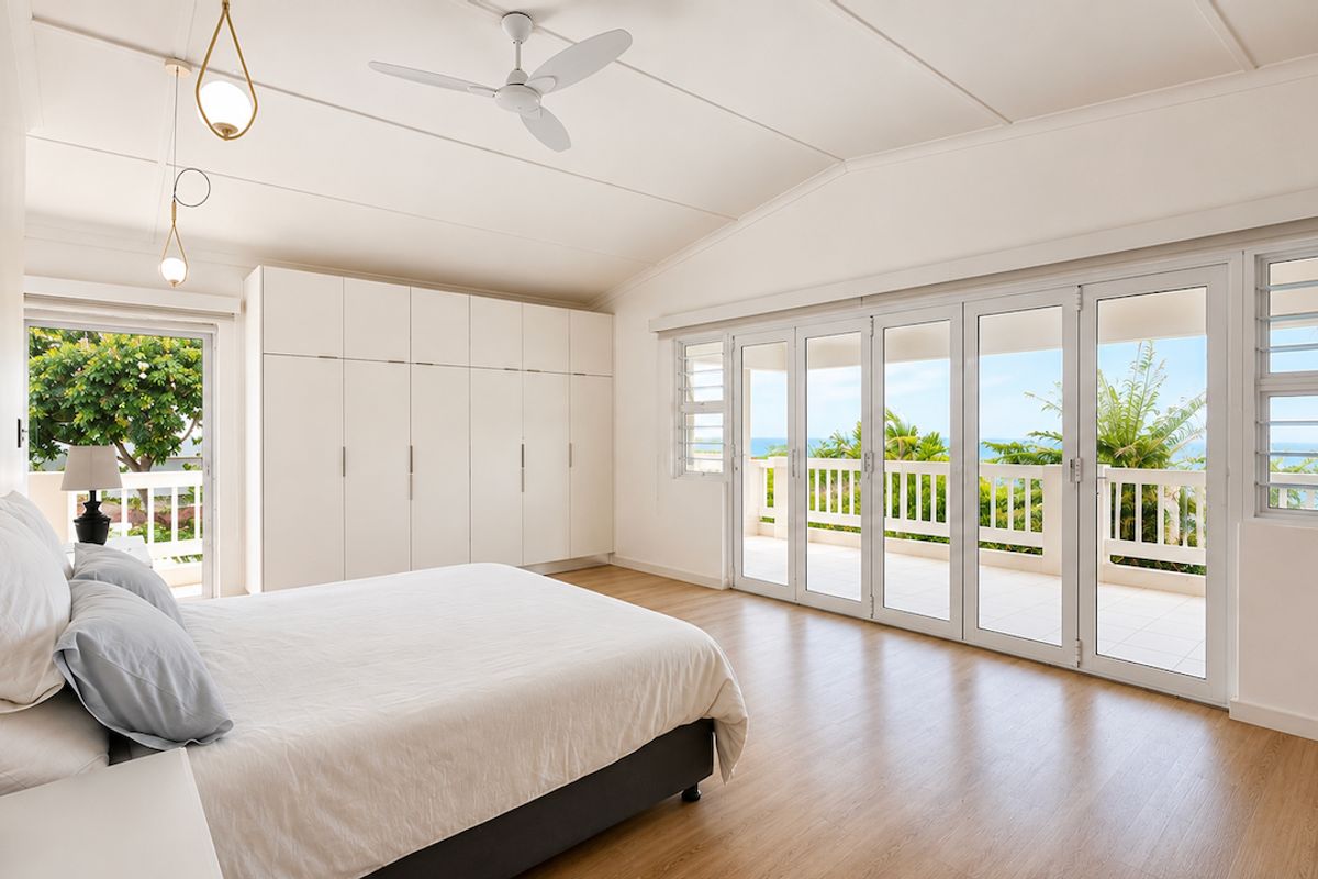 Spacious bedroom featuring vaulted ceilings, built-in wardrobes, and large bifold doors opening onto a balcony with ocean views.