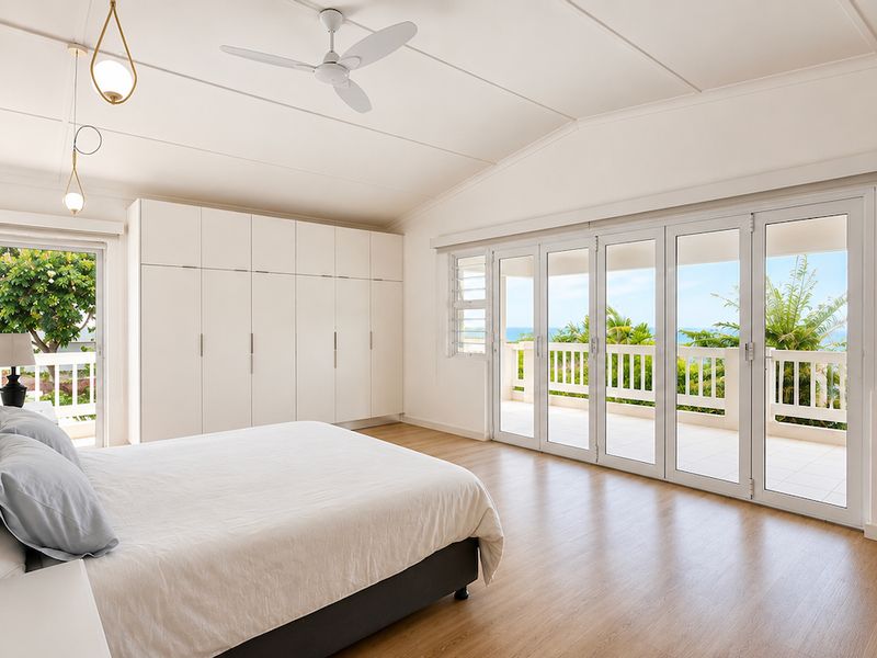 Spacious bedroom featuring vaulted ceilings, built-in wardrobes, and large bifold doors opening onto a balcony with ocean views.