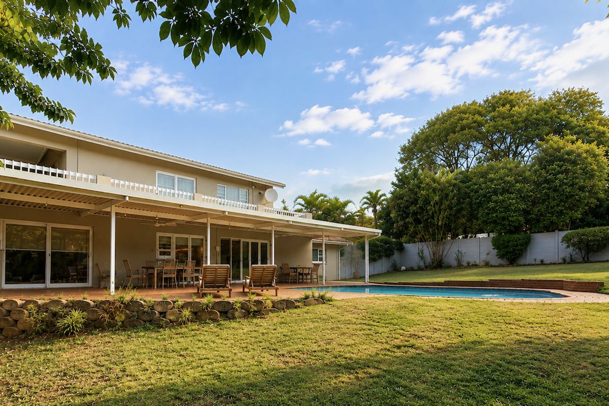 Spacious rear exterior featuring a covered patio, swimming pool, and a well-maintained garden with a retaining wall and perimeter fencing.