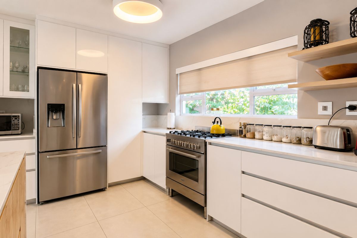 Modern kitchen featuring white gloss cabinetry, stone countertops, stainless steel appliances, and floating timber shelving with ample natural light.