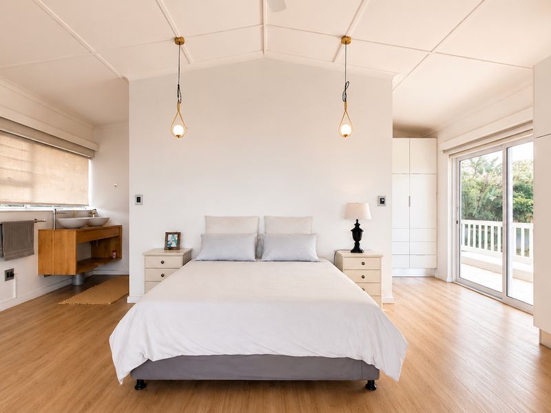 Spacious bedroom featuring built-in wardrobes, timber-look flooring, a private vanity area, and sliding glass doors leading to an outdoor balcony.