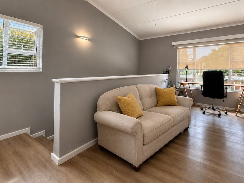 A bright and well-maintained living area featuring laminate flooring, neutral wall tones, and natural light through large windows with fitted blinds.