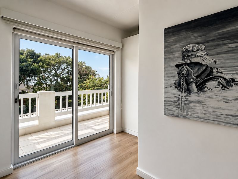 Bright bedroom featuring laminate flooring, built-in cupboards, and a sliding glass door providing direct access to a private balcony.