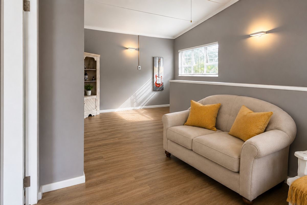 A bright and well-maintained living area featuring modern laminate flooring, neutral grey walls, and wall-mounted lighting fixtures.