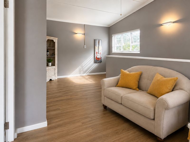 A bright and well-maintained living area featuring modern laminate flooring, neutral grey walls, and wall-mounted lighting fixtures.