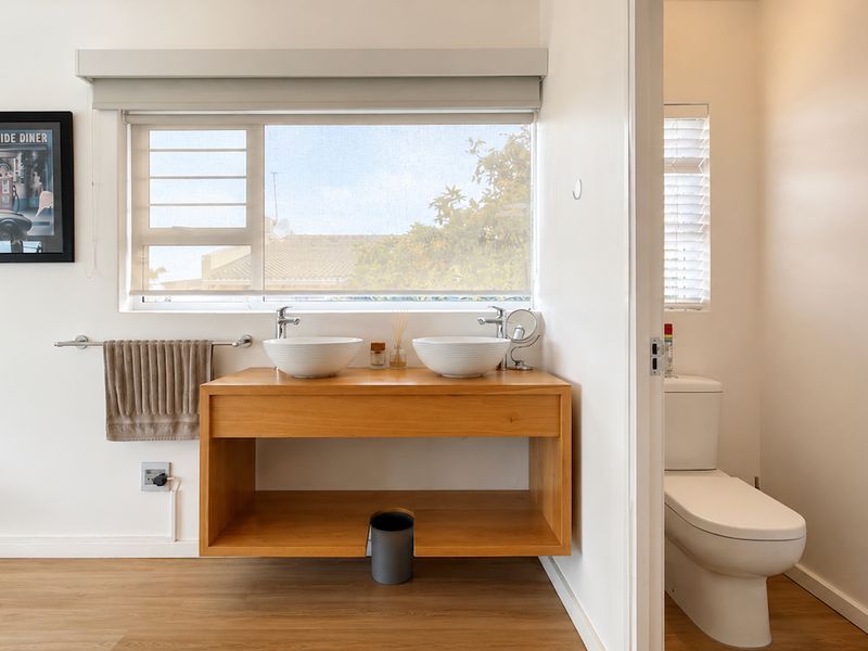 Modern bathroom featuring a double vessel sink vanity with wooden cabinetry and a separate enclosed toilet area with light laminate flooring.