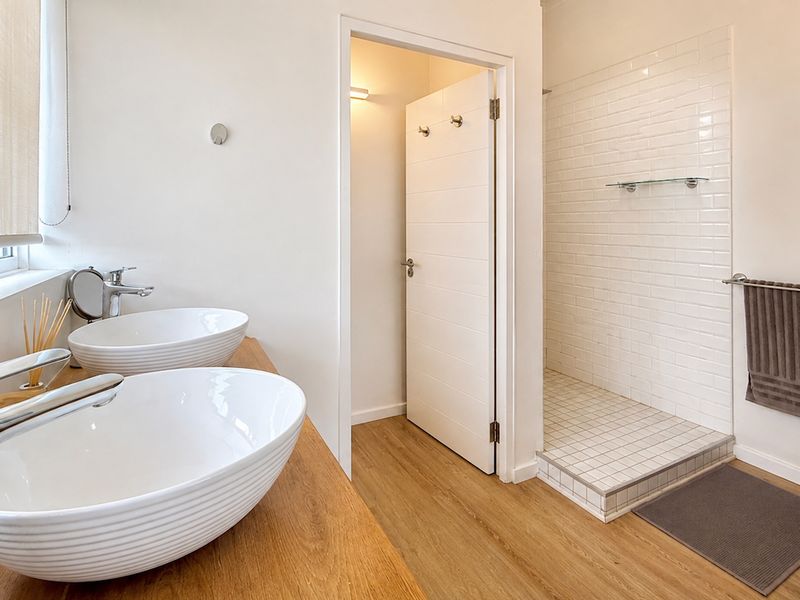 Modern bathroom featuring a double vanity with vessel sinks, timber-look countertop, and a walk-in shower with white subway tiling.