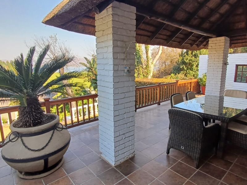 A covered outdoor patio featuring a thatched roof, brick pillars, and a wooden balustrade, offering an open space for outdoor dining and relaxation.