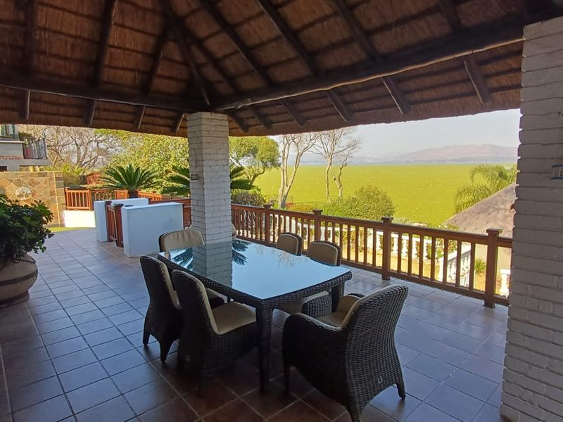Covered outdoor patio featuring a traditional thatched roof, brick pillars, and tiled flooring, offering scenic views of the surrounding landscape.