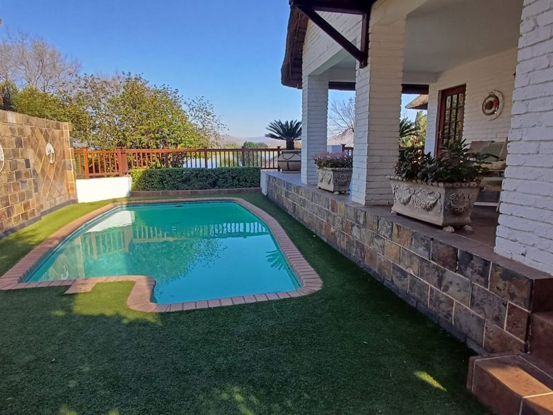 Outdoor pool area featuring a swimming pool, stone-clad retaining walls, and a covered patio with brick pillars overlooking the garden.