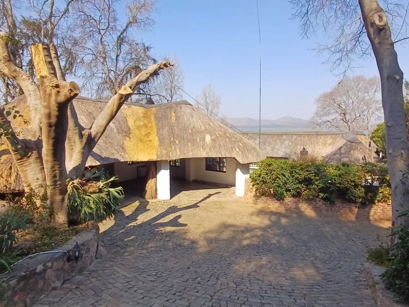 Front exterior view of a property featuring a traditional thatched roof, cobblestone driveway, and established garden surroundings.