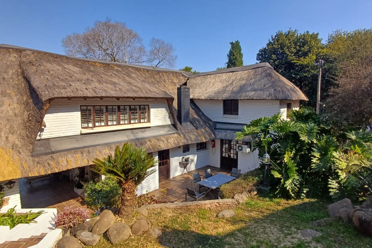Rear view of a traditional thatched-roof house featuring a tiled patio area and established garden surroundings.
