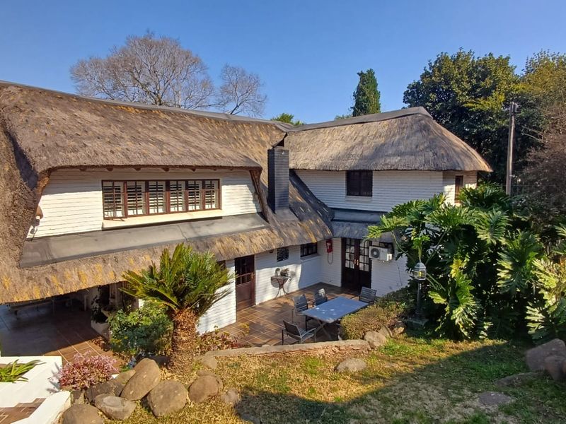 Rear view of a traditional thatched-roof house featuring a tiled patio area and established garden surroundings.