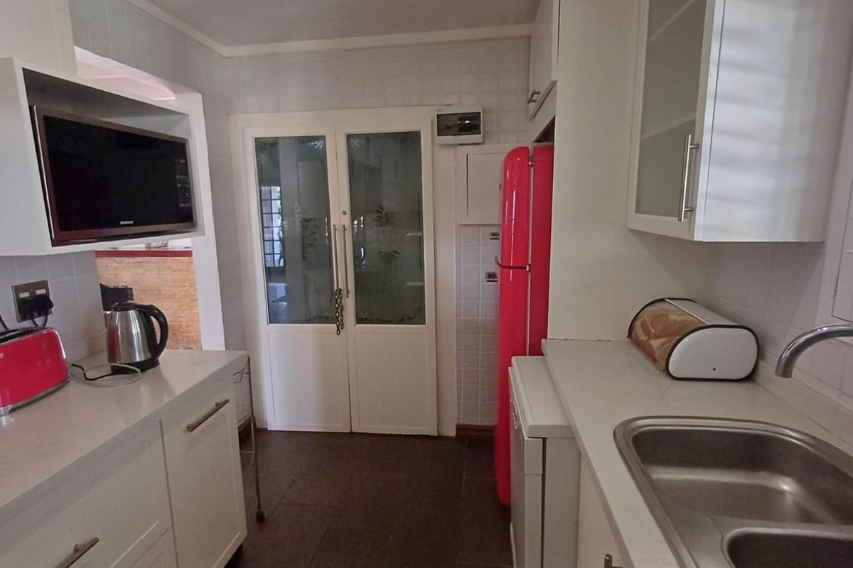 A functional kitchen featuring white cabinetry, tiled splashbacks, a double basin sink, and built-in microwave, offering a clean and practical workspace.