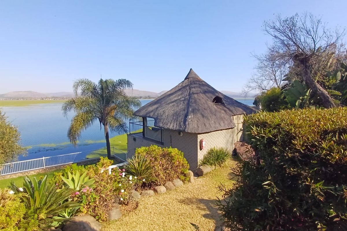 A scenic rear view of a property featuring a traditional thatch roof structure, established garden, and direct views over the adjacent lake.