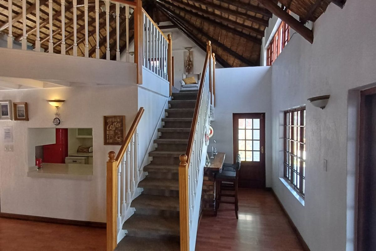 Spacious living area featuring a prominent timber staircase, mezzanine level, exposed thatched roof rafters, and a convenient pass-through window to the kitchen.