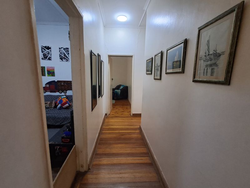A functional hallway featuring original timber flooring and neutral wall finishes, providing access to adjacent living spaces.