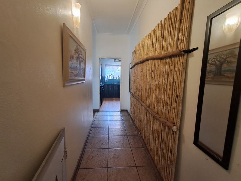 A tiled hallway leading to a kitchen area, featuring neutral walls and fixed lighting fixtures.