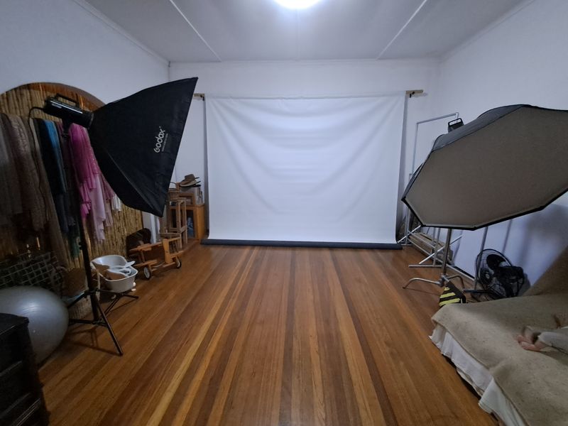 A spacious room featuring polished hardwood flooring and a distinctive arched wall detail, currently utilized as a studio space.