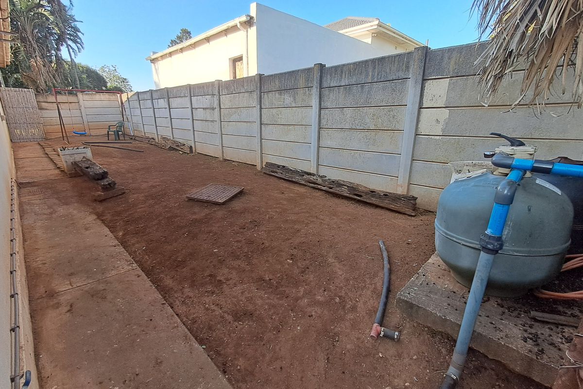 A rear exterior area featuring a precast concrete boundary wall, pool filtration equipment, and an unlandscaped yard space requiring ground cover or garden development.