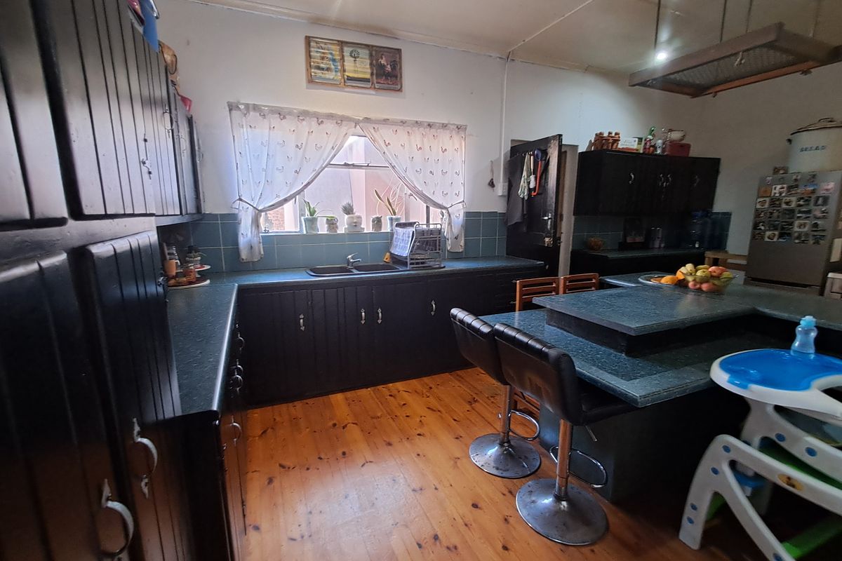 A functional kitchen featuring dark built-in cabinetry, a central island, double sink, and warm timber flooring, offering a classic layout with potential for modernization.