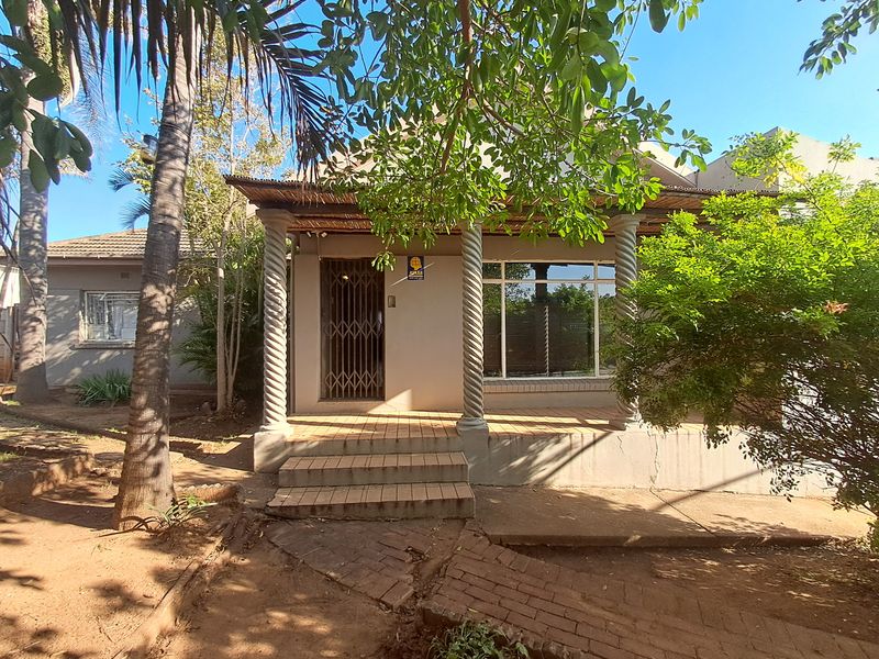 Front facade of the house featuring a covered porch with decorative spiral columns, brick steps, and a secure entrance gate.