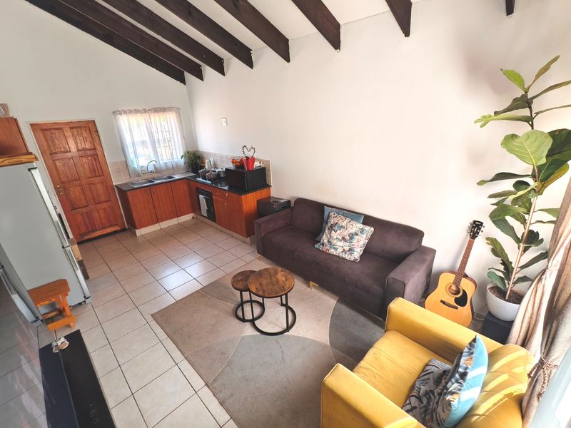 Open-plan living area featuring exposed timber ceiling beams, tiled flooring, and a compact kitchen with built-in cabinetry and integrated appliances.