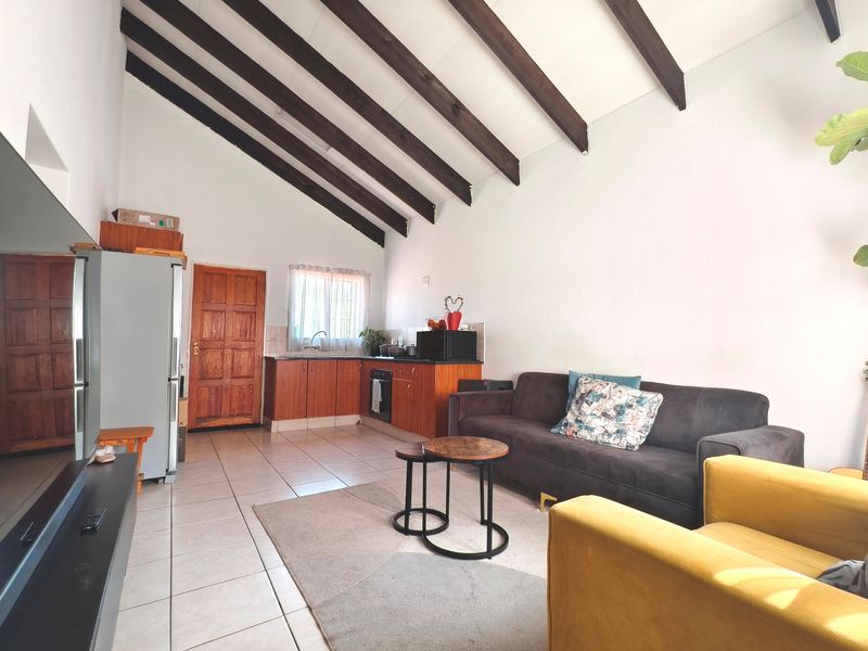 Open-plan living area featuring a vaulted ceiling with exposed timber beams, tiled flooring, and a functional kitchen with built-in cabinetry and oven.
