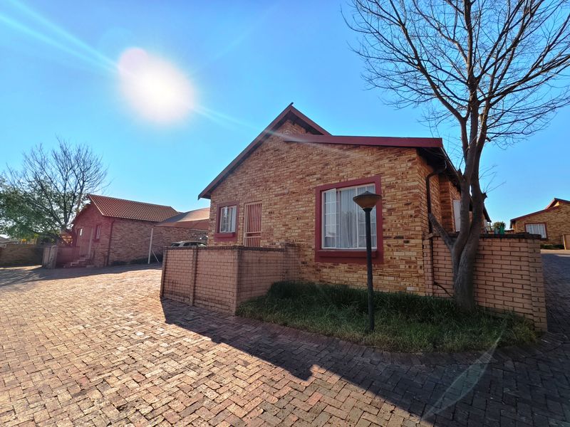 A well-maintained facebrick townhouse exterior featuring a paved driveway, secure boundary wall, and tiled roof in a residential complex setting.