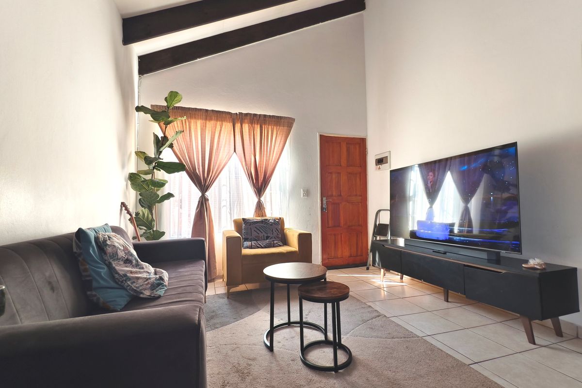A living room featuring high ceilings with exposed timber beams, tiled flooring, and a solid timber entrance door.