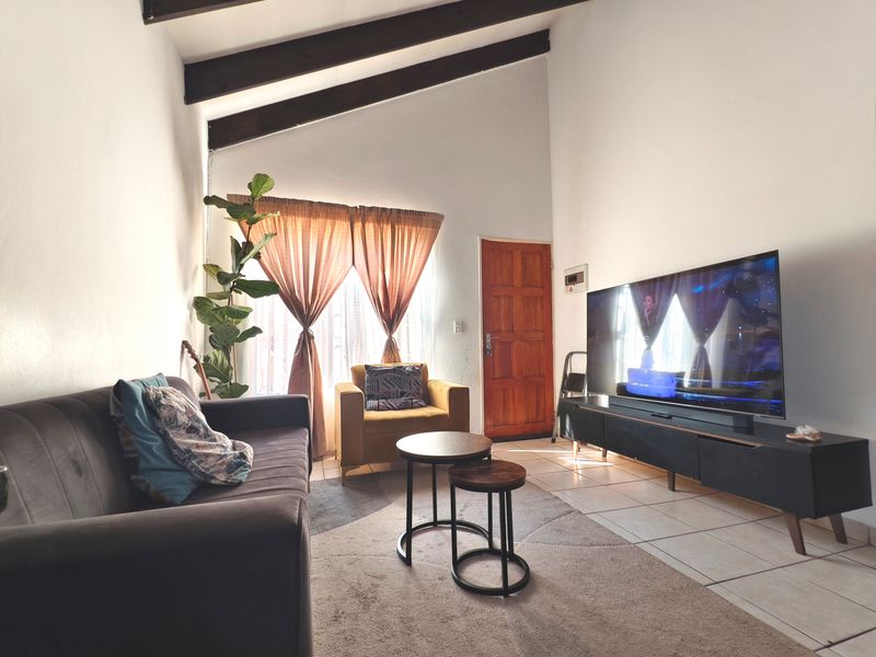 A living room featuring high ceilings with exposed timber beams, tiled flooring, and a solid timber entrance door.