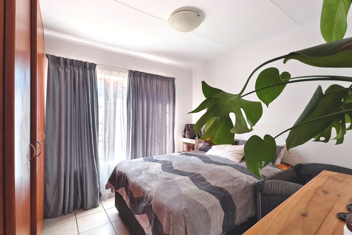 A functional bedroom featuring tiled flooring, a built-in wardrobe, and large windows with curtains, providing a comfortable and practical living space.
