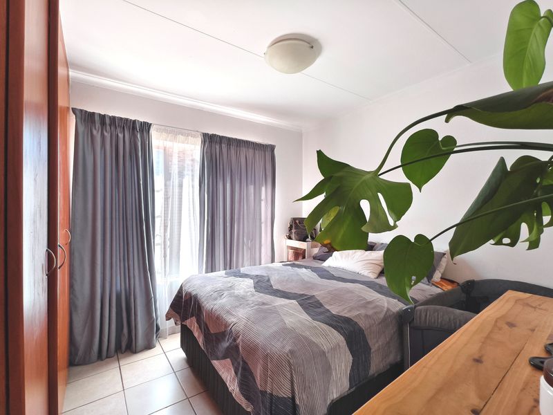 A functional bedroom featuring tiled flooring, a built-in wardrobe, and large windows with curtains, providing a comfortable and practical living space.