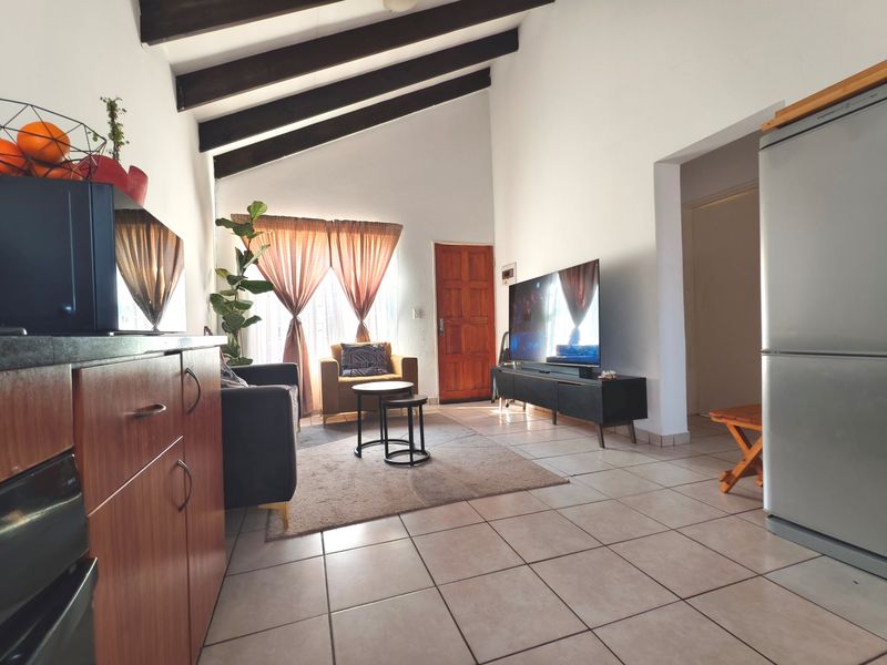 Open-plan living area featuring vaulted ceilings with exposed timber beams and tiled flooring, creating a bright and spacious atmosphere.