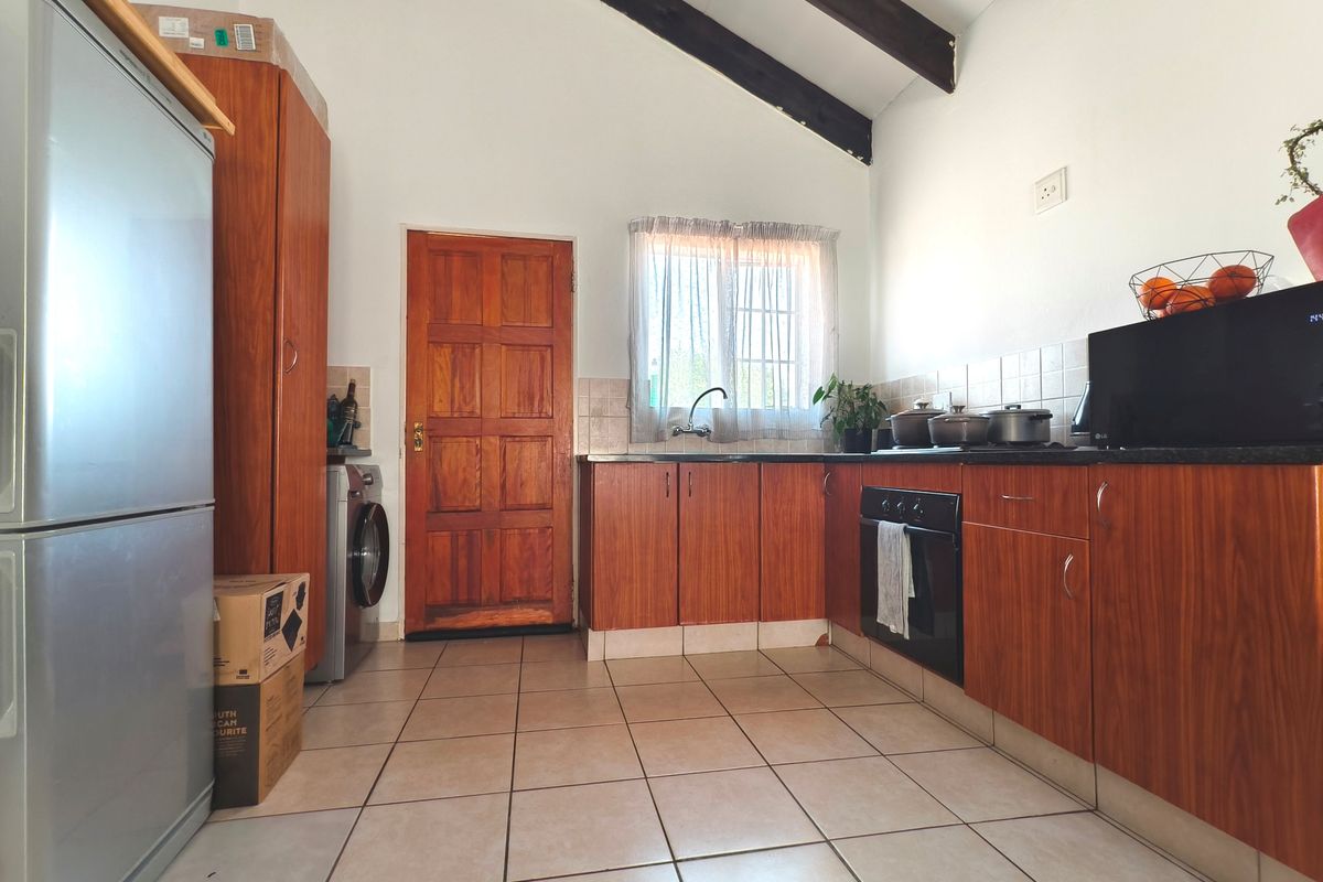 A functional kitchen featuring wooden cabinetry, tiled flooring, exposed timber ceiling beams, and a built-in oven with direct access to an exterior door.
