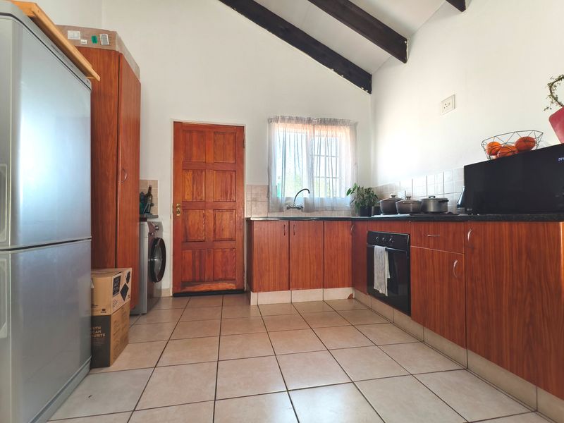 A functional kitchen featuring wooden cabinetry, tiled flooring, exposed timber ceiling beams, and a built-in oven with direct access to an exterior door.