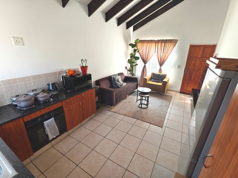 Open-plan living area featuring a kitchen with granite countertops, built-in oven, hob, and exposed timber ceiling beams, creating a functional and connected living space.